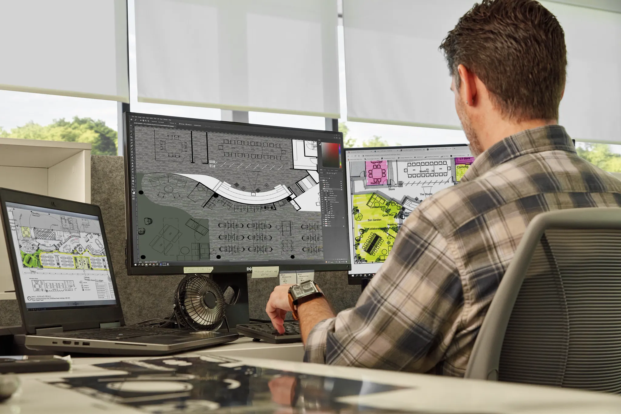 Man working at a desk with multiple computer monitors displaying architectural designs in a modern office setting