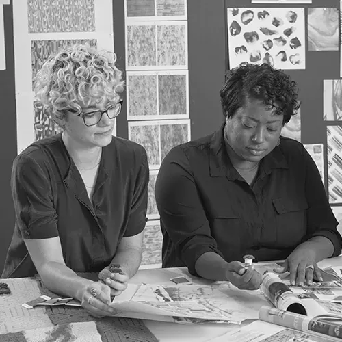 Two women collaborating on design projects with flooring samples and design sketches in an office setting