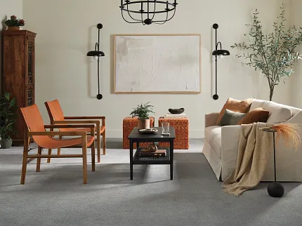 Contemporary living room with gray flooring and stylish furniture arrangement Modern living room with gray soft surface flooring, featuring a beige sofa, orange chairs, and a black coffee table