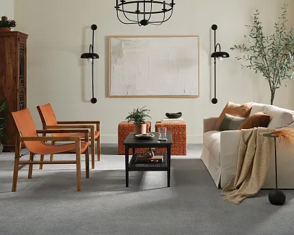 Contemporary living room with gray flooring and stylish furniture arrangement Modern living room with gray soft surface flooring, featuring a beige sofa, orange chairs, and a black coffee table