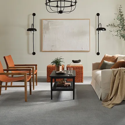 Contemporary living room with gray flooring and stylish furniture arrangement Modern living room with gray soft surface flooring, featuring a beige sofa, orange chairs, and a black coffee table