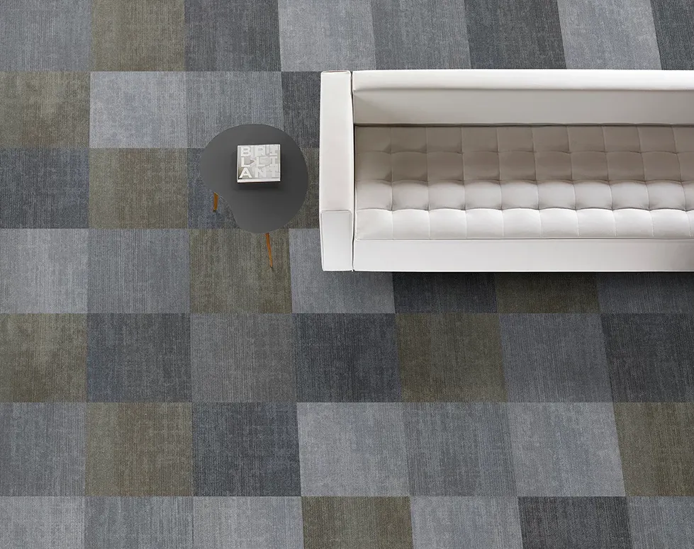 Modern living room with a white sofa and a round side table on a checkered pattern commercial carpet tile in shades of gray and olive green