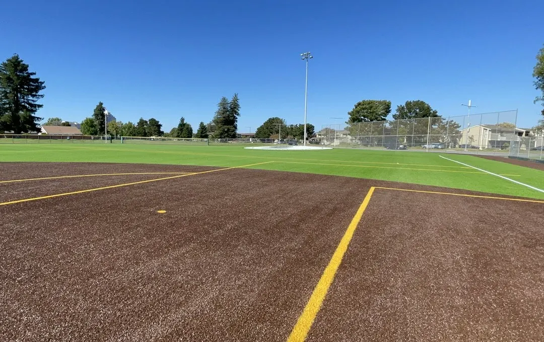 Artificial turf baseball field with brown and green sections under clear blue sky