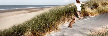 Scenic beach walk with woman and dog Woman and dog walking on a sandy beach with grassy dunes