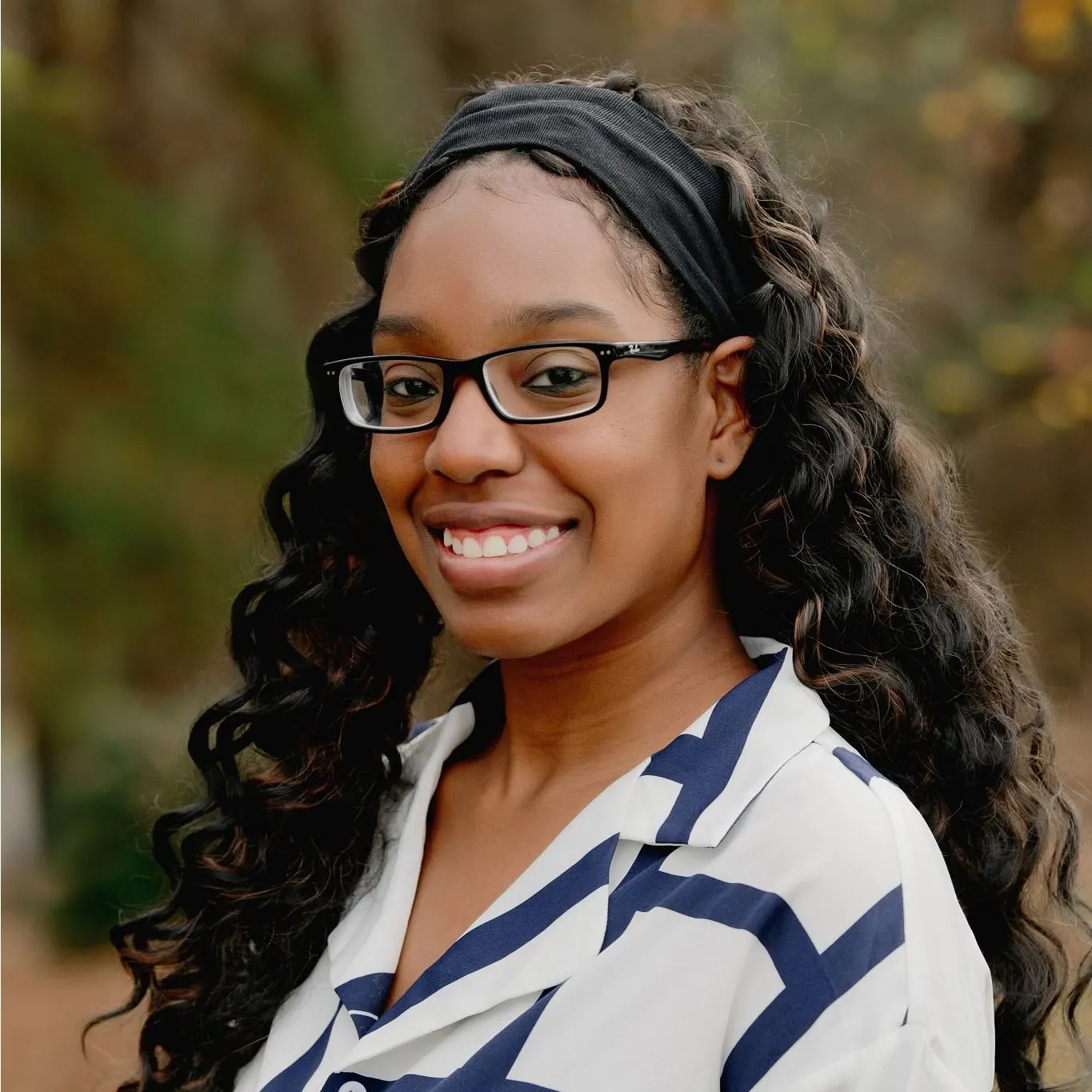 Woman with long curly hair wearing a white and blue striped shirt in an outdoor setting