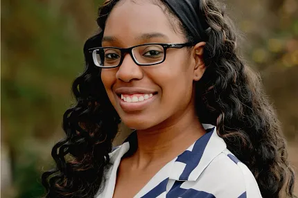 Outdoor portrait of a woman with long curly hair and a white and blue striped shirt Woman with long curly hair wearing a white and blue striped shirt in an outdoor setting