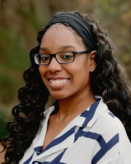 Outdoor portrait of a woman with long curly hair and a white and blue striped shirt Woman with long curly hair wearing a white and blue striped shirt in an outdoor setting