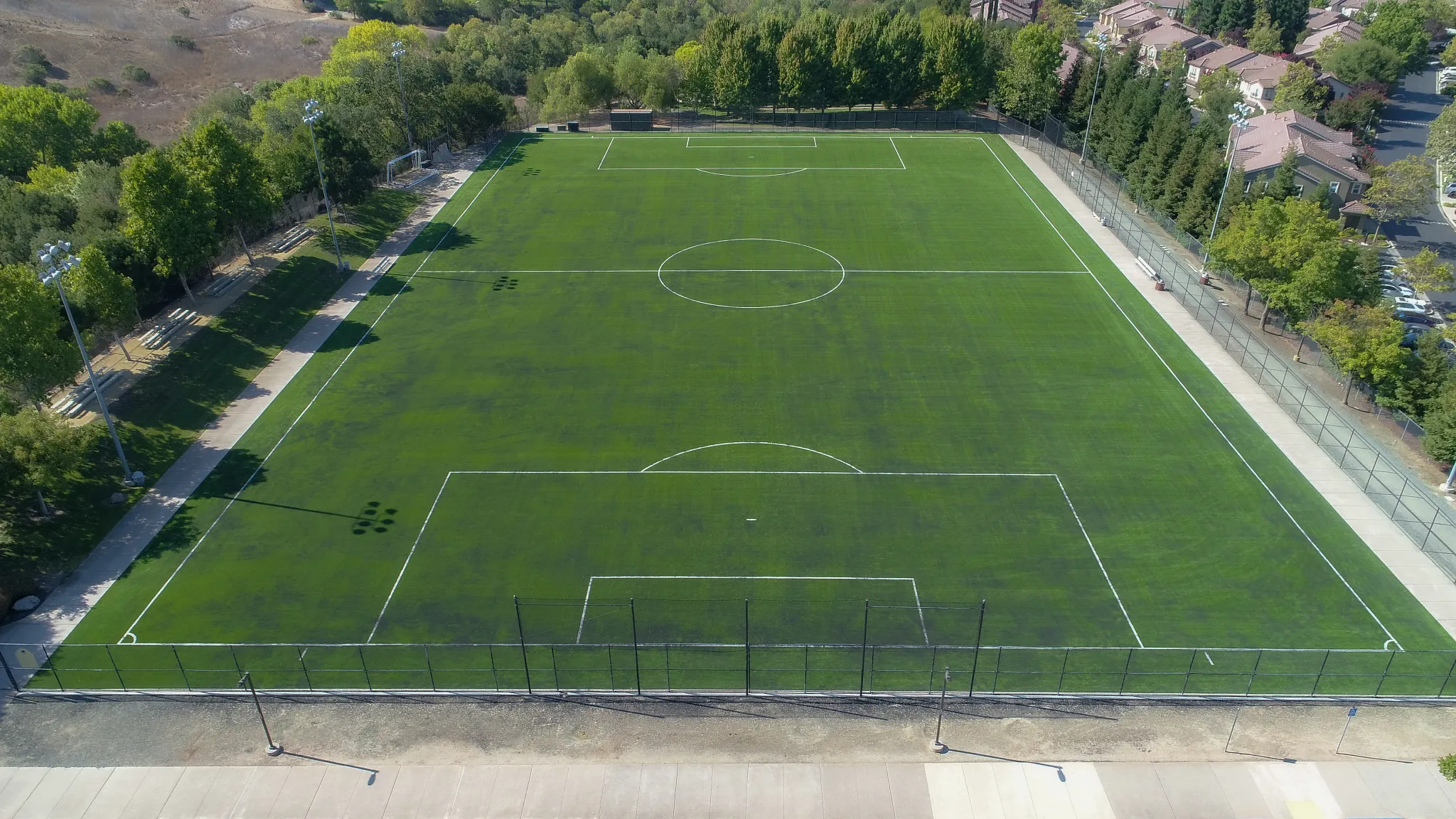 Aerial view of a large artificial turf soccer field surrounded by trees and pathways
