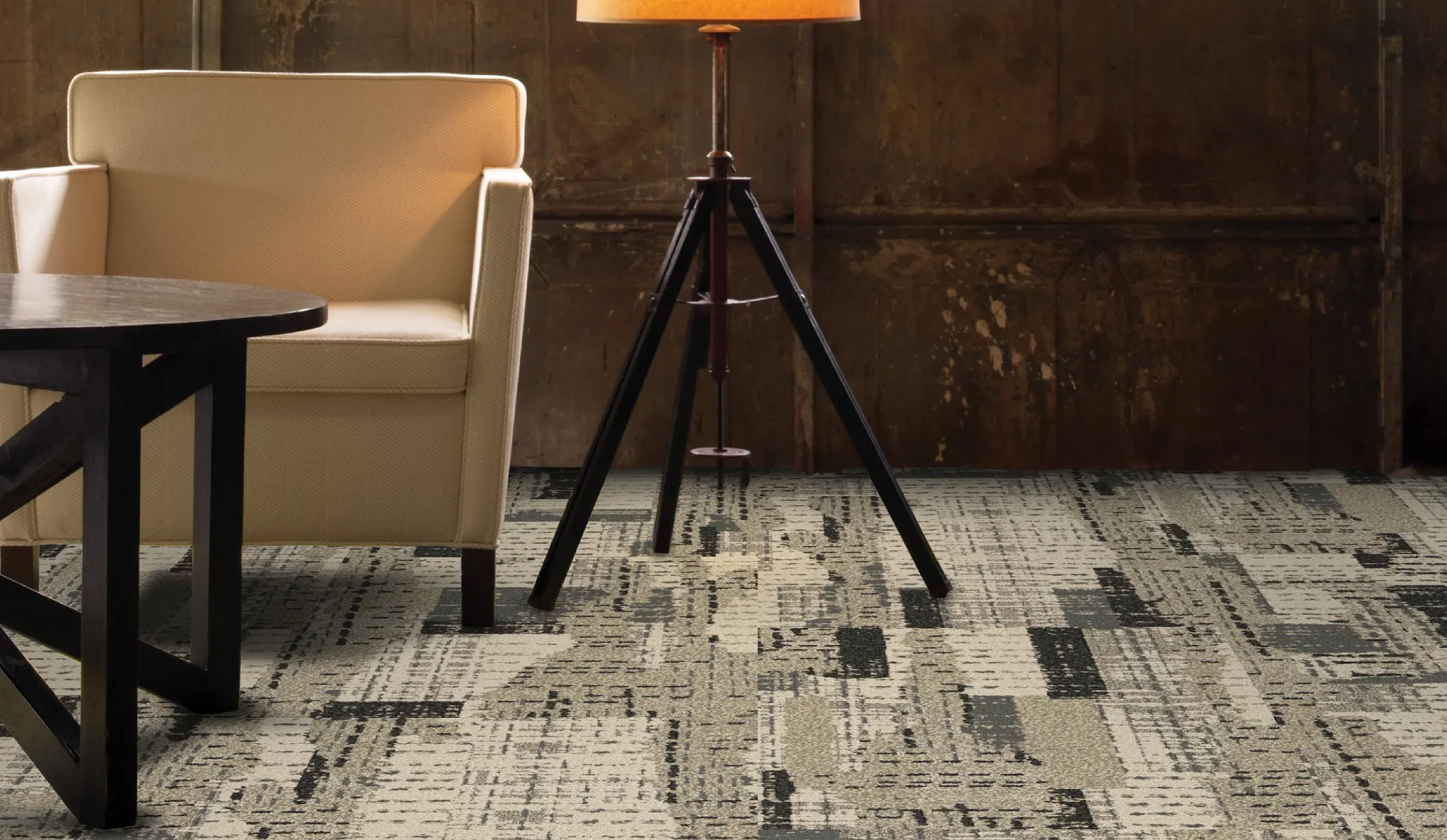 Modern living room with beige armchair, wooden coffee table, and tripod lamp on patterned commercial carpet tile