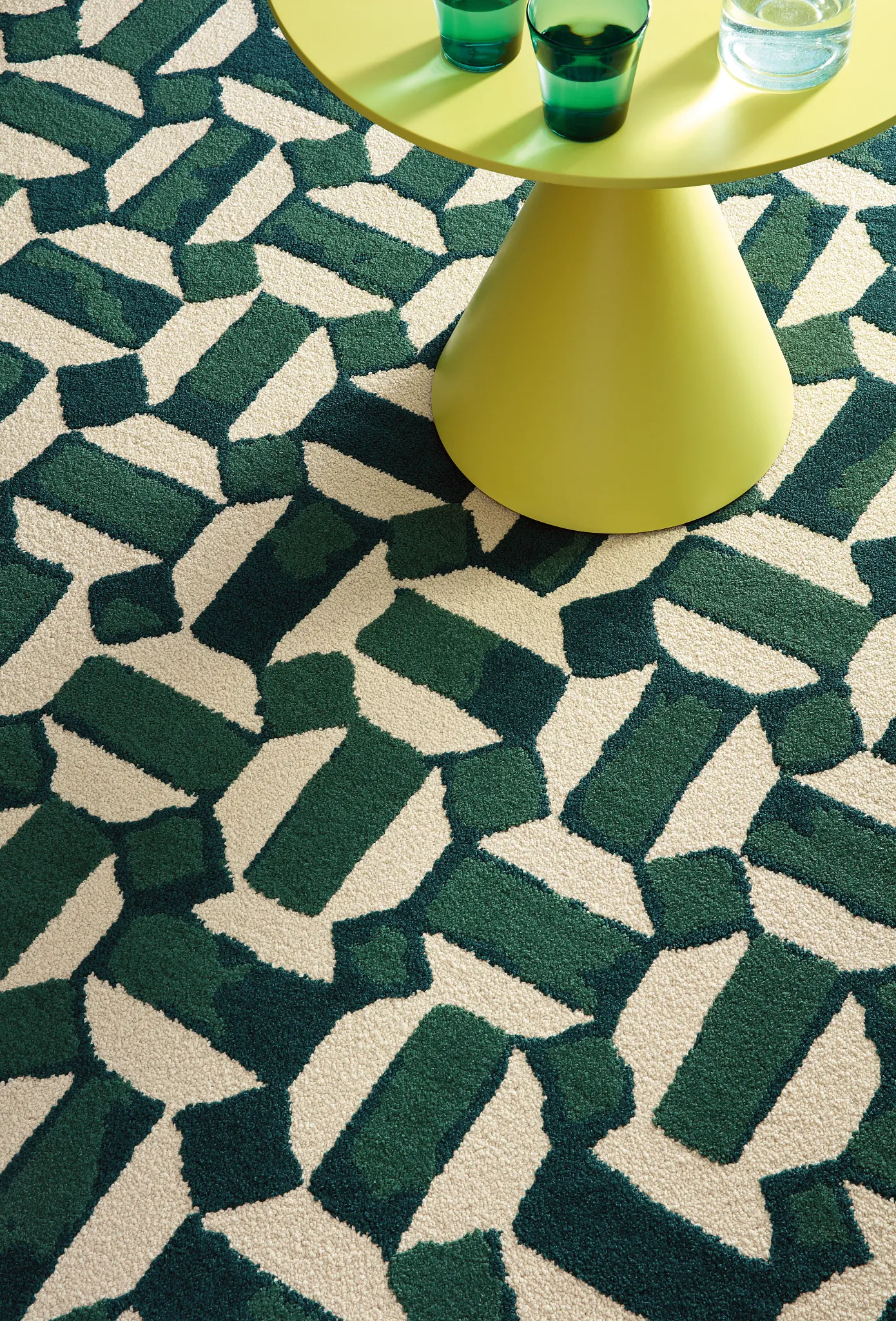 Geometric patterned commercial carpet tile in green and cream with a modern yellow table and green glasses