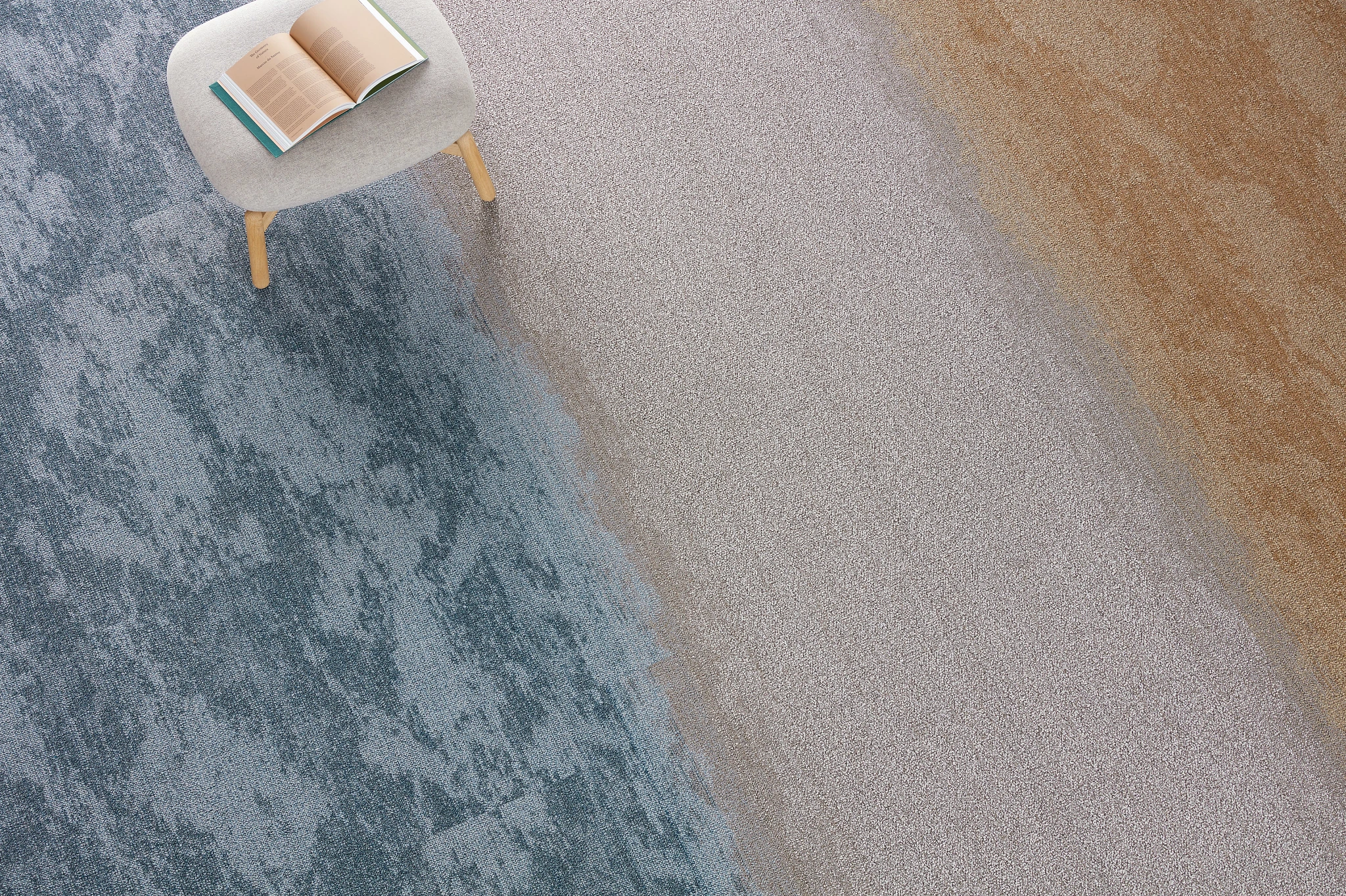 Modern room scene with a gradient carpet in blue, gray, and beige tones, featuring a small stool with an open book