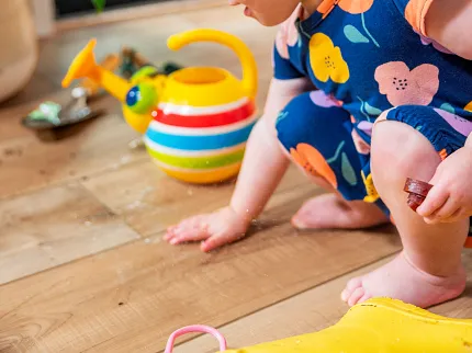 Coretec Residential WPC Wood Look Vinyl Flooring - Durable and Pet Friendly Child playing on Coretec Residential WPC flooring with wood look, featuring a colorful watering can and vibrant floral outfit, 48.03x7.09 inch dimensions