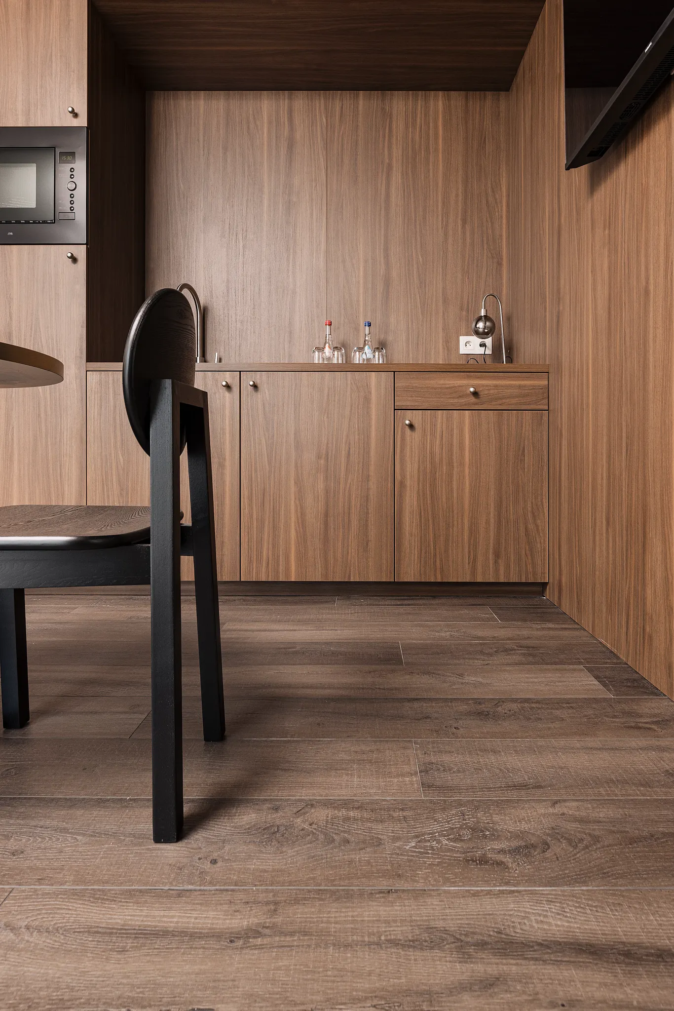 Modern chair in hotel room with walnut kitchen cabinets and dark wooden Coretec floor