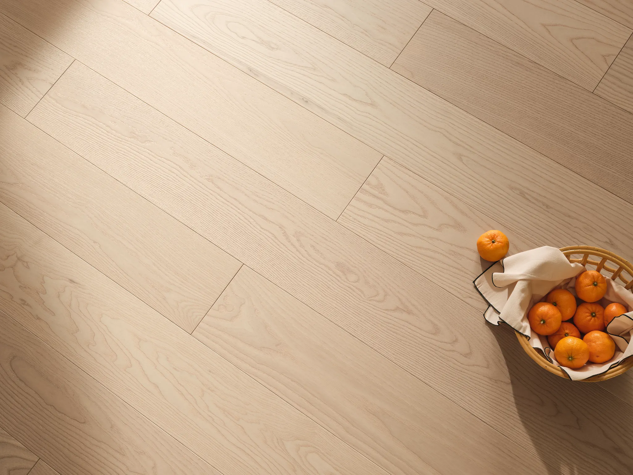 Overhead view of blonde hardwood flooring with a basket of oranges sitting on top.
