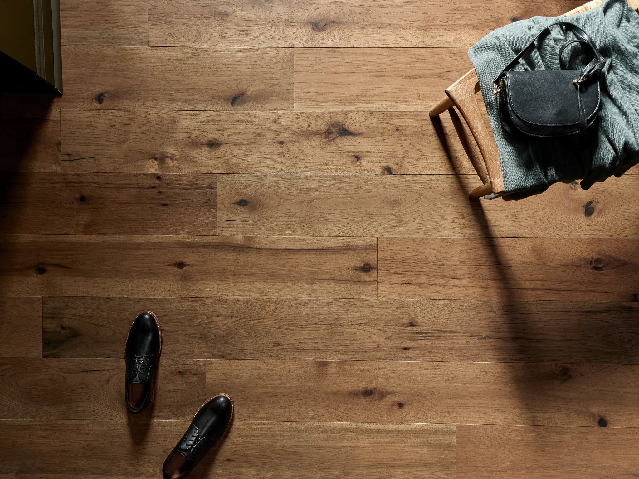 Hardwood flooring with natural wood grain and knots, featuring a pair of black shoes and a chair with a bag and blanket