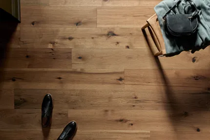 Elegant Hardwood Flooring with Natural Wood Grain and Knots Hardwood flooring with natural wood grain and knots, featuring a pair of black shoes and a chair with a bag and blanket
