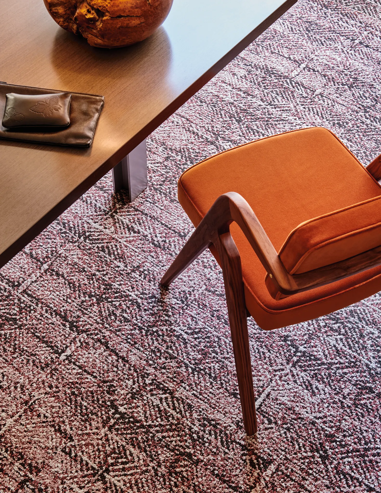 Modern office setting with a wooden table and orange chair on a patterned commercial carpet tile floor