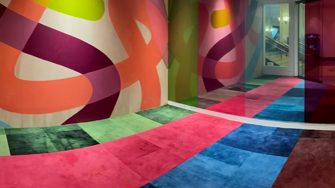 corridor with glass mirrors, blue carpet tile, green carpet tile, pink carpet tile, and purple carpet tile