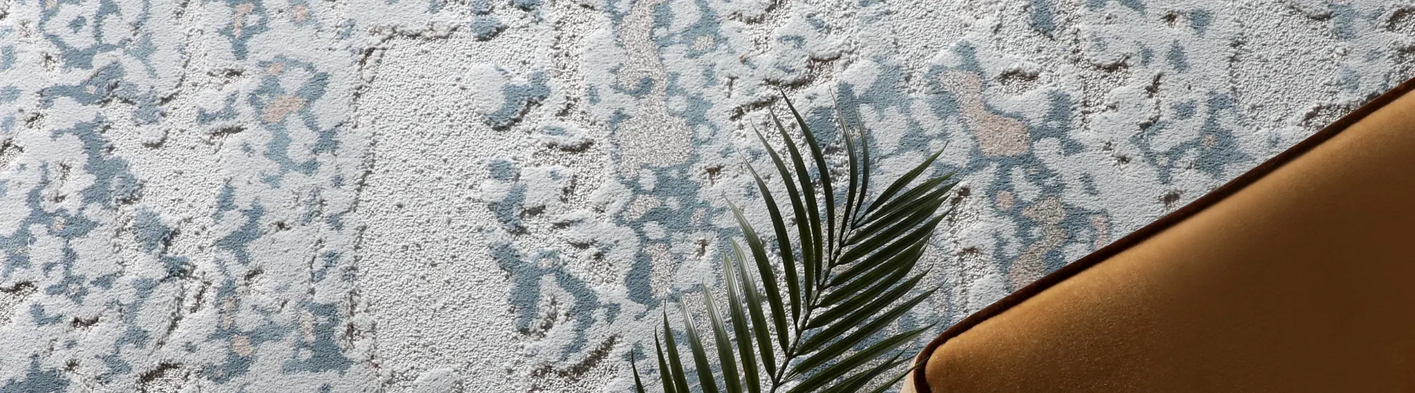 Abstract patterned carpet in blue and beige tones with a palm leaf and brown chair