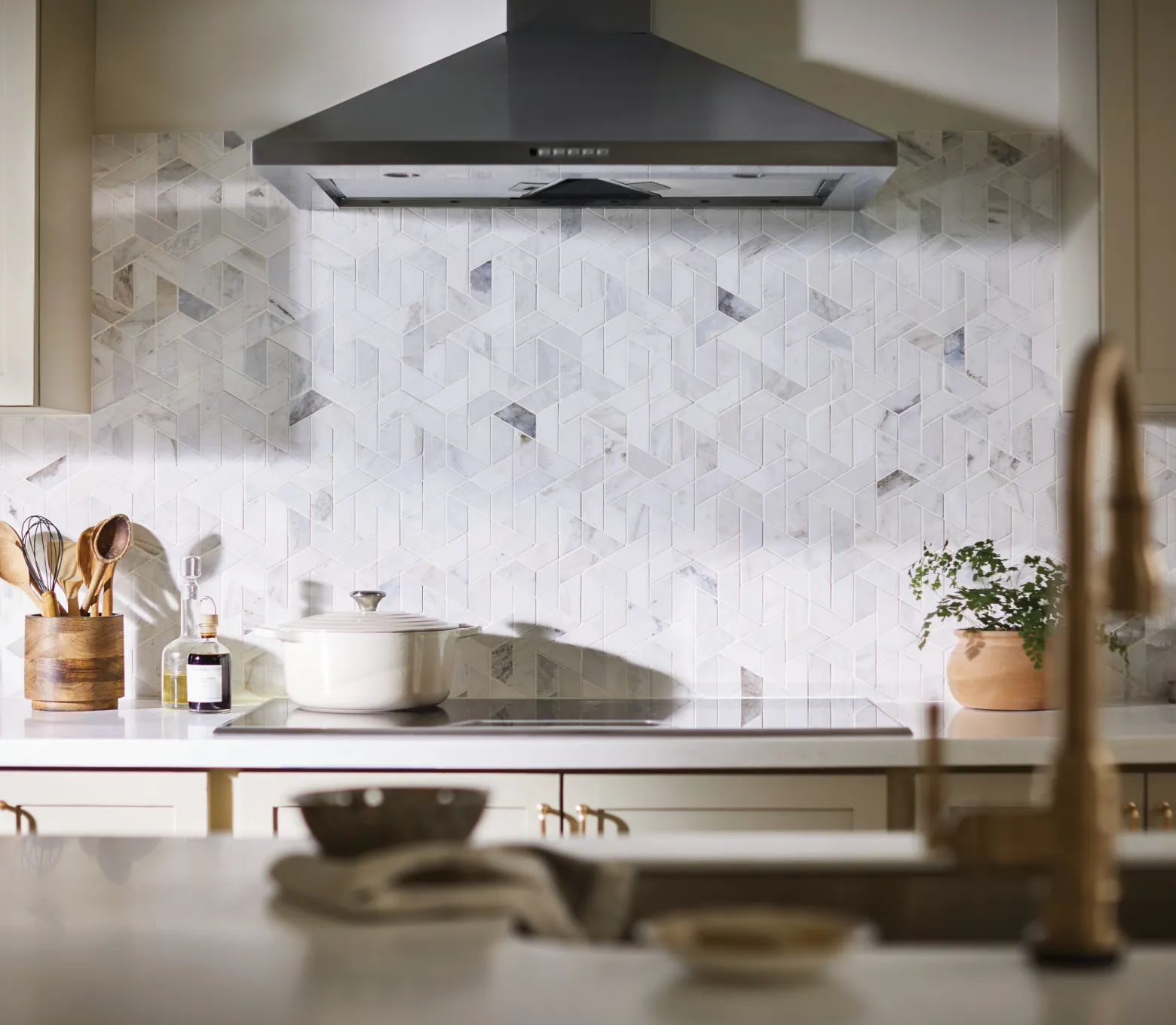 Modern kitchen with geometric patterned tile backspash in neutral tones, featuring a sleek black range hood and white cabinetry