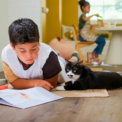 Wood Look Luxury Vinyl Plank Flooring in a Family Room Scene Child reading with a cat on wood look luxury vinyl plank flooring in a bright room