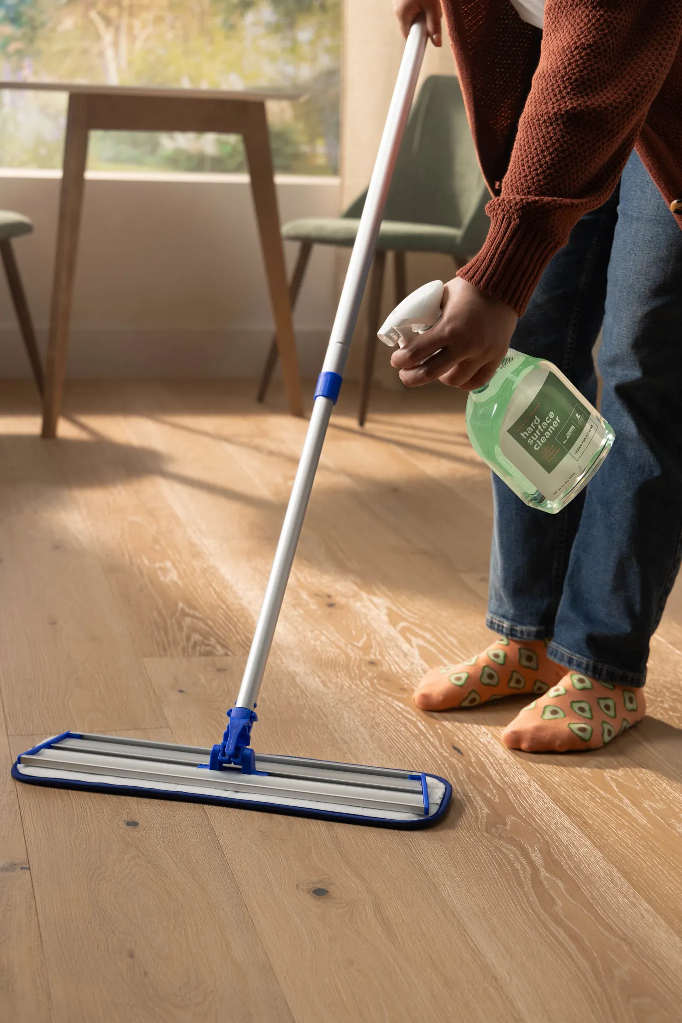 Person cleaning light wood flooring with mop and hard surface cleaner in a cozy home setting