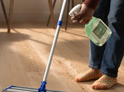 Easy-to-Maintain Light Wood Flooring for Everyday Comfort Person cleaning light wood flooring with mop and hard surface cleaner in a cozy home setting