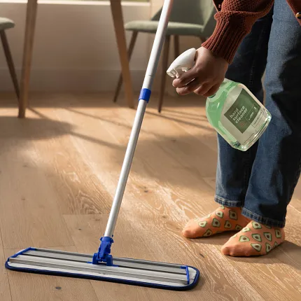 Easy-to-Maintain Light Wood Flooring for Everyday Comfort Person cleaning light wood flooring with mop and hard surface cleaner in a cozy home setting