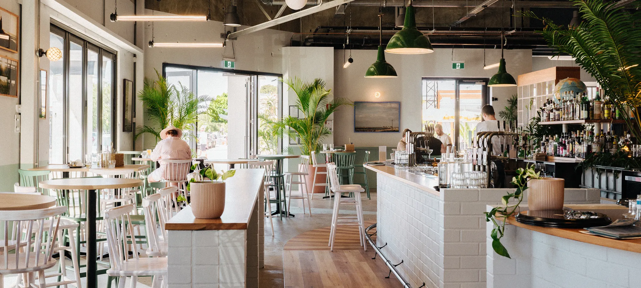 Light-filled café and hospitality interior at Busselton Pavilion featuring timber flooring, white tiled bar, indoor planting and contemporary seating in Western Australia