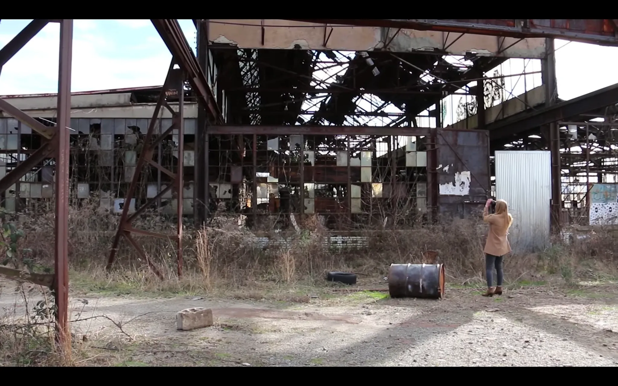 Woman photographing an abandoned industrial building with overgrown vegetation