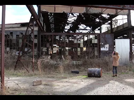 Abandoned Industrial Building Photography Scene Woman photographing an abandoned industrial building with overgrown vegetation