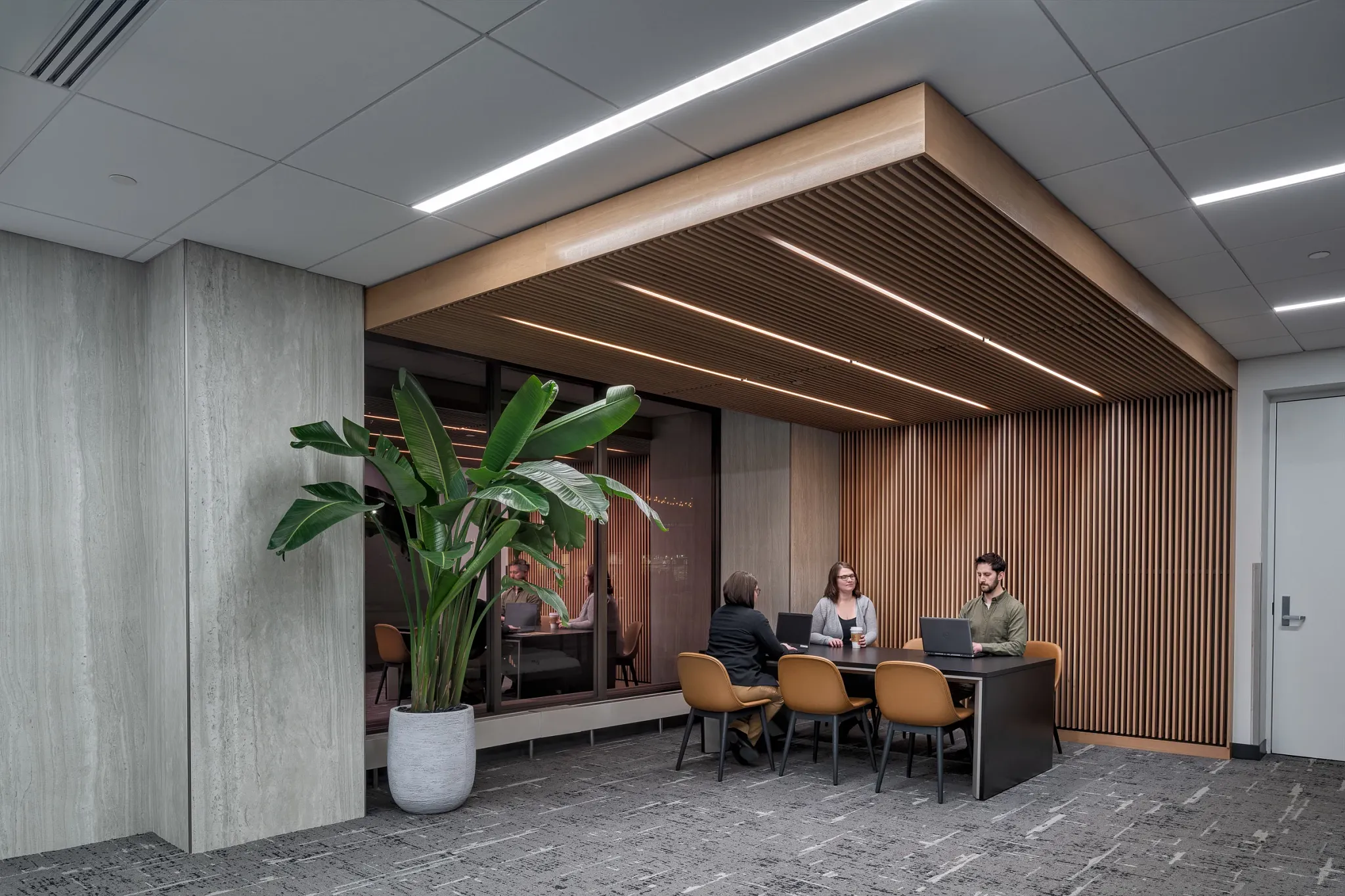 Modern workplace setting with commercial carpet tile flooring, featuring a group of professionals in a meeting area with wooden slat ceiling and large potted plant