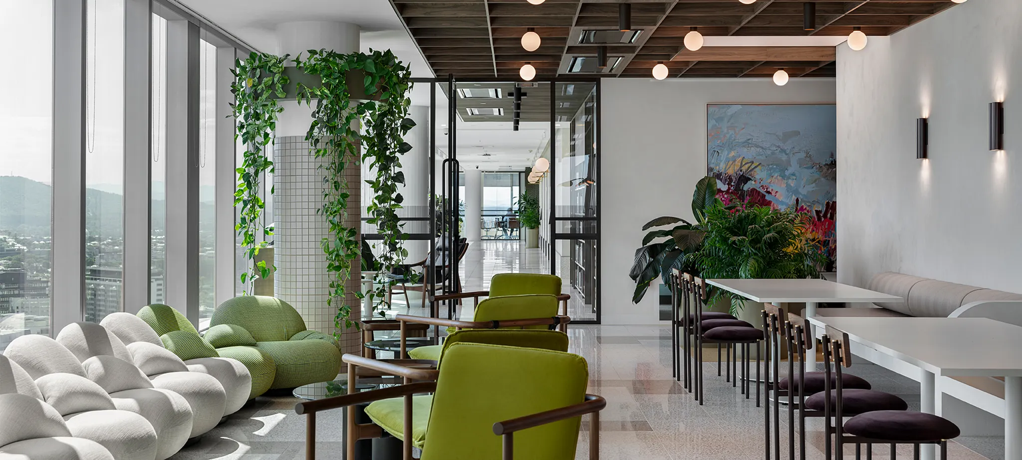 Modern workplace lounge area with green and white seating, large windows, and indoor plants