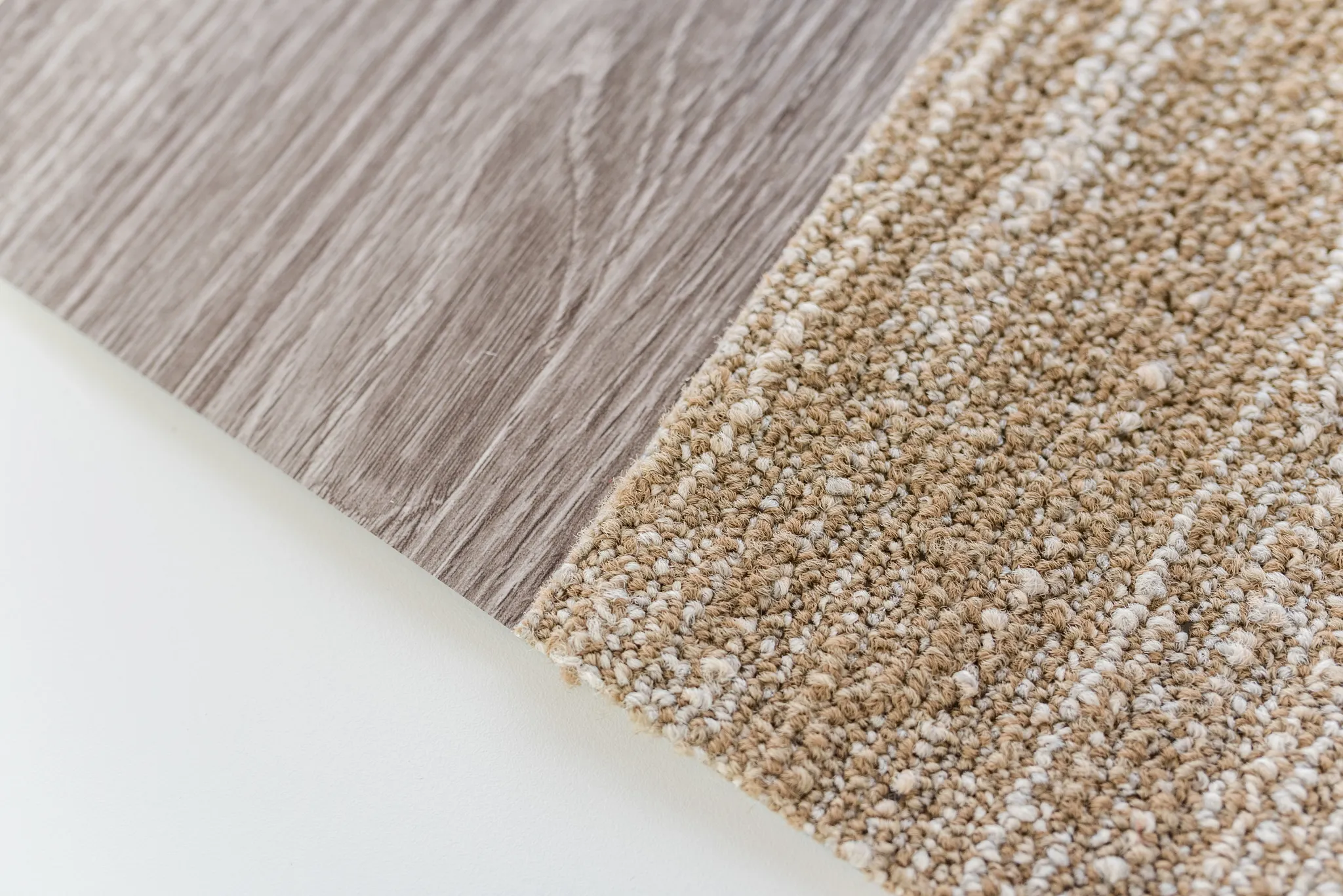 Close-up of a flooring swatch featuring a light brown wood-look vinyl and a beige textured carpet tile