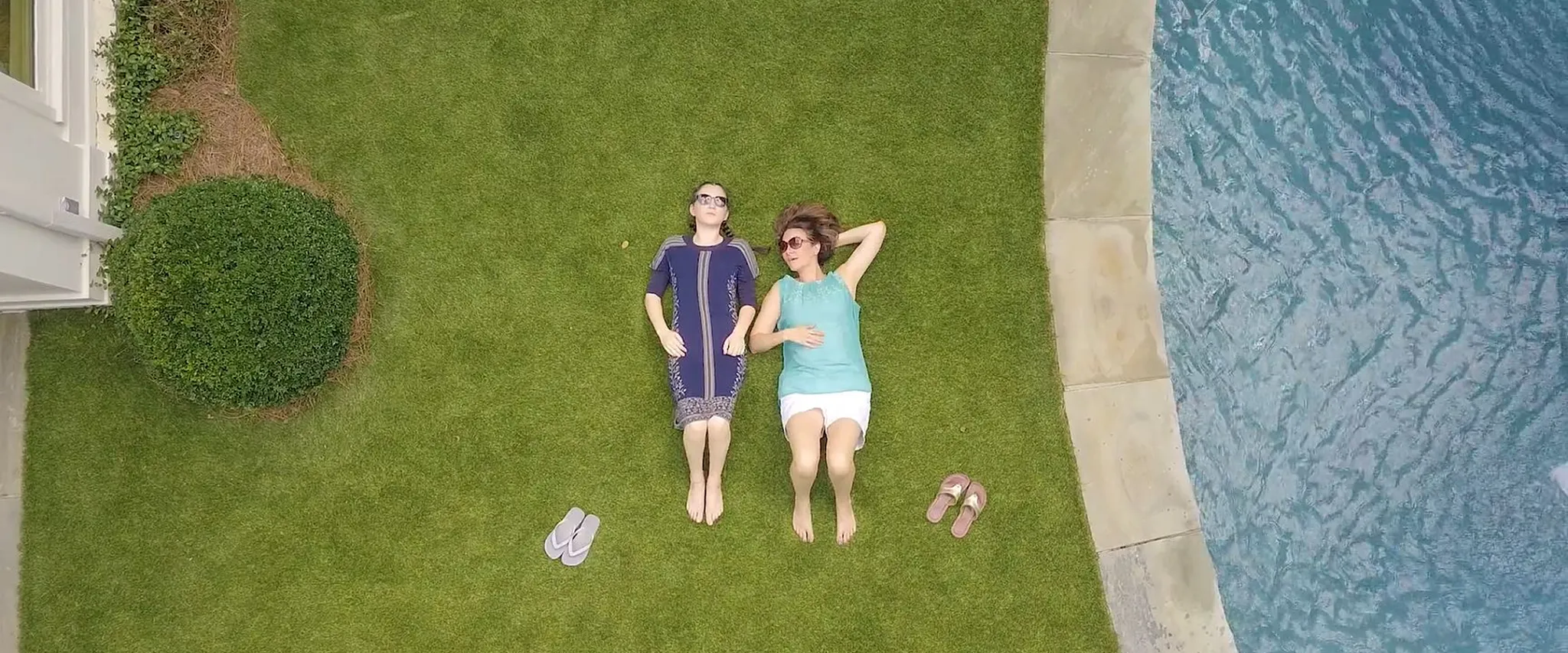 Two people relaxing on green grass by a poolside