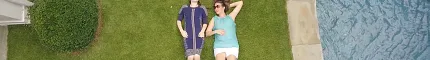 Two people relaxing on green grass by a poolside