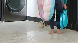 A child in a swimsuit standing in a water puddle in a laundry room