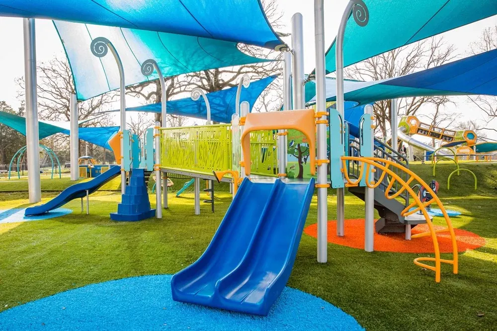 Colorful playground with blue slide and shade structures installed over artificial turf and impact-absorbing safety surface.