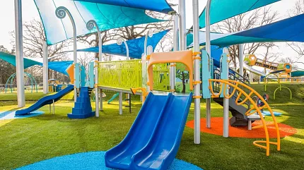 Playground Artificial Turf Installation with Safety Surfacing Colorful playground with blue slide and shade structures installed over artificial turf and impact-absorbing safety surface.