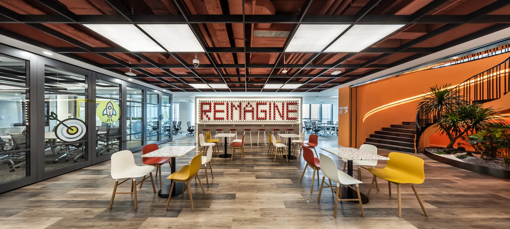 Espacio de trabajo moderno con piso COREtec de construcción SPC multicapa y base de corcho integrada, formato de 48.03 x 7.17 pulgadas, en un entorno de oficina vibrante y colaborativo con sillas coloridas y un letrero con la palabra "Reimagine".