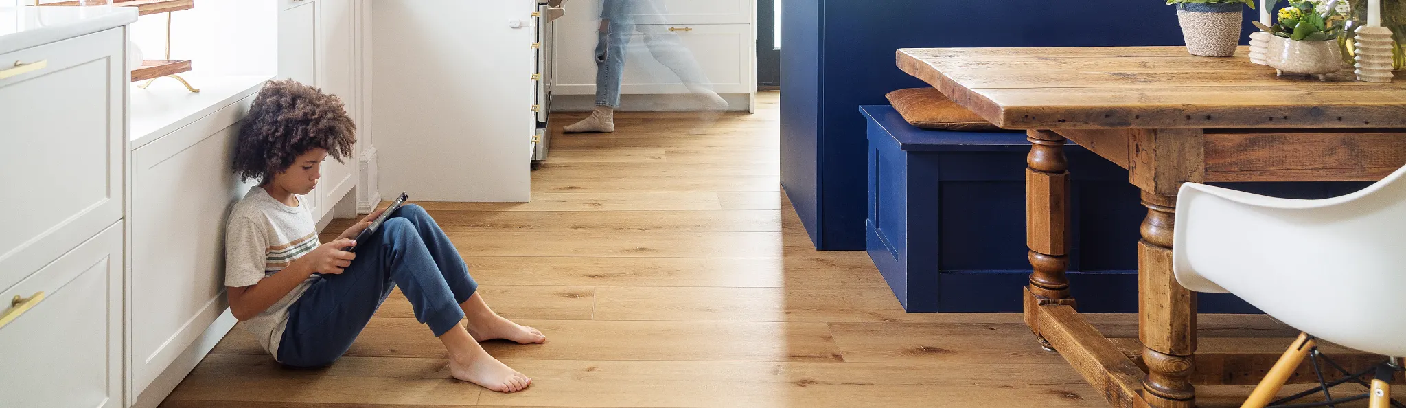 Modern kitchen with wood look luxury vinyl plank flooring and a child sitting on the floor using a tablet