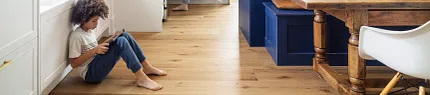 Wood Look Luxury Vinyl Plank Flooring in Modern Kitchen Scene Modern kitchen with wood look luxury vinyl plank flooring and a child sitting on the floor using a tablet