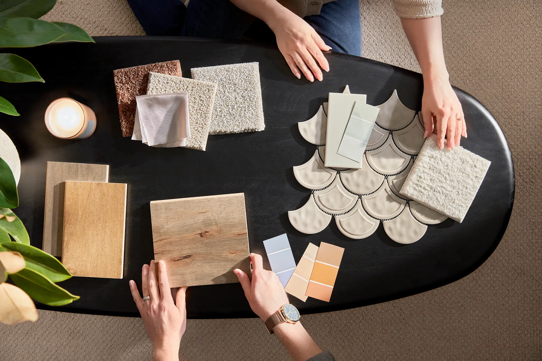 Overhead view of two people selecting flooring samples including carpet, hardwood, and tile on a black table