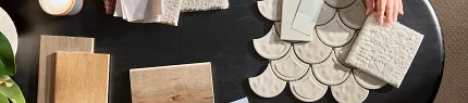 Flooring selection process with carpet, hardwood, and tile samples for a comfortable home ambiance Overhead view of two people selecting flooring samples including carpet, hardwood, and tile on a black table