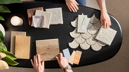 Flooring selection process with carpet, hardwood, and tile samples for a comfortable home ambiance Overhead view of two people selecting flooring samples including carpet, hardwood, and tile on a black table