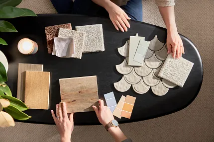 Flooring selection process with carpet, hardwood, and tile samples for a comfortable home ambiance Overhead view of two people selecting flooring samples including carpet, hardwood, and tile on a black table