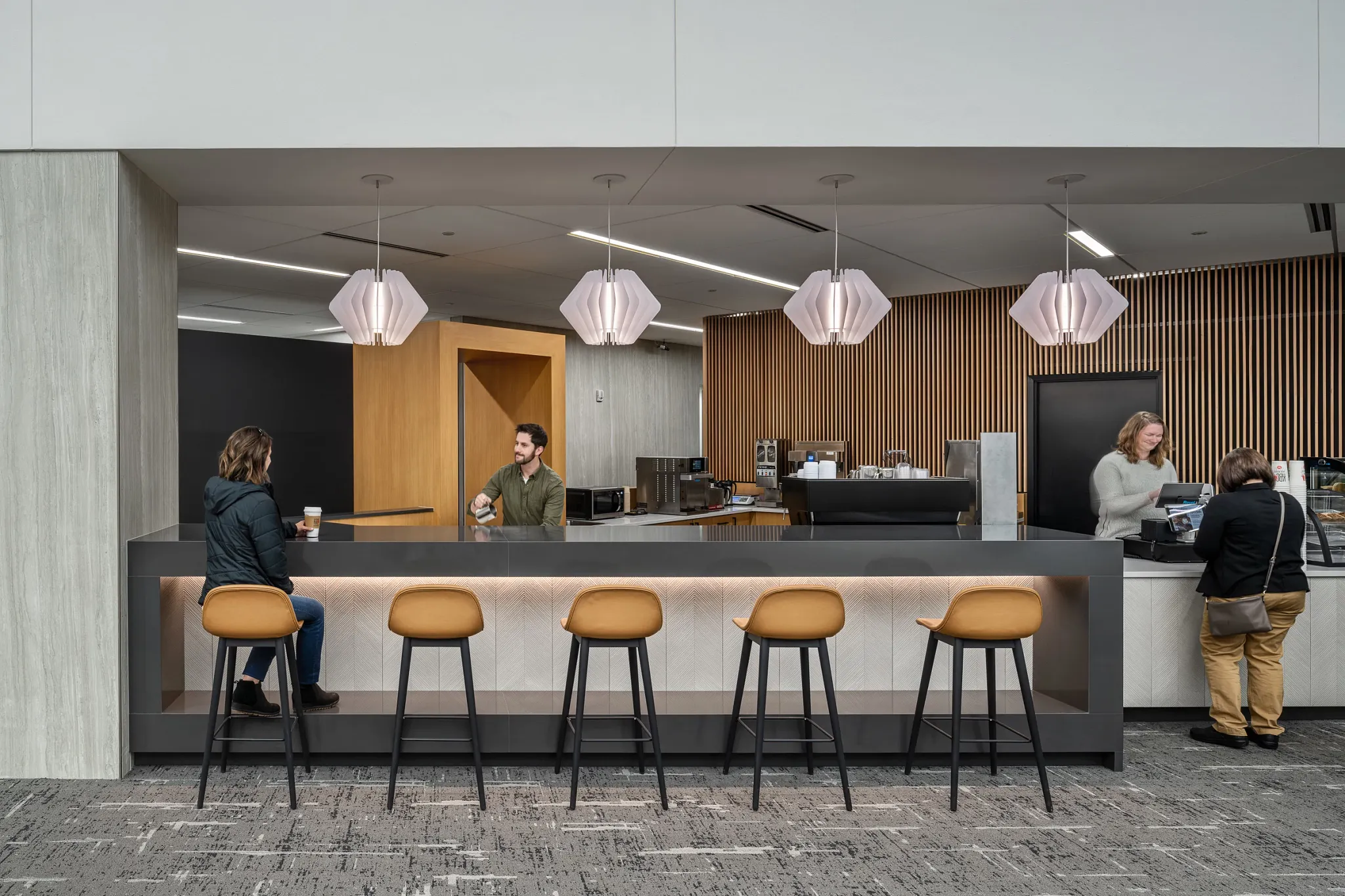 Modern workplace lounge area with commercial carpet tile flooring, featuring a bar counter with stools and pendant lighting