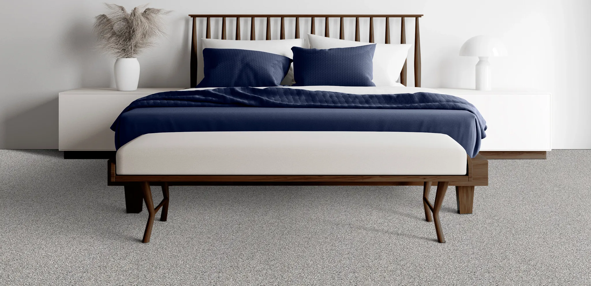 Modern bedroom with a wooden bed frame, white bedding, and blue pillows on a speckled commercial carpet floor