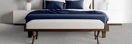 Modern Bedroom with Commercial Carpet Flooring Modern bedroom with a wooden bed frame, white bedding, and blue pillows on a speckled commercial carpet floor